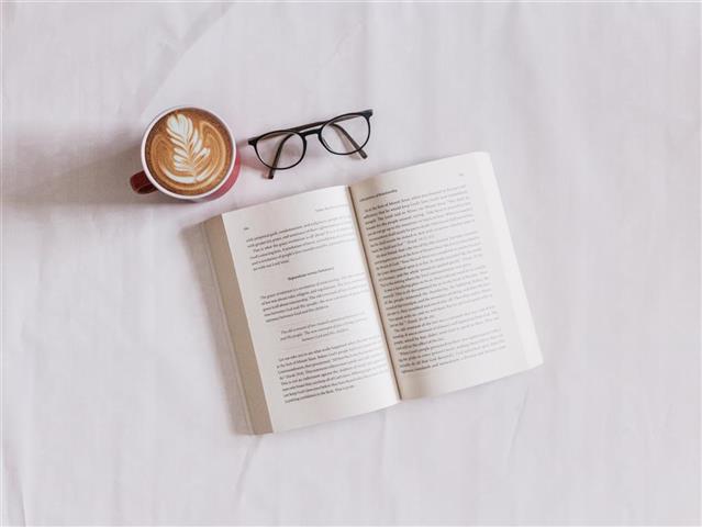 Otwarta książka, okulary i kawa z mlekiem na białym tle