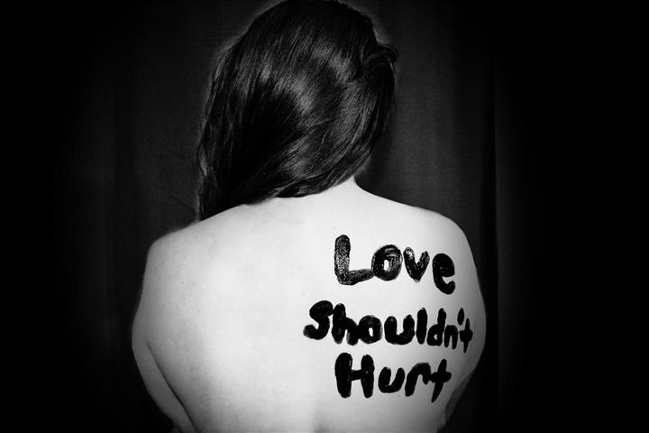 czarno-białe zdjęcie kobiety odwróconej plecami, na których napisano miłość nie powinna boleć, autor Sydney Sims